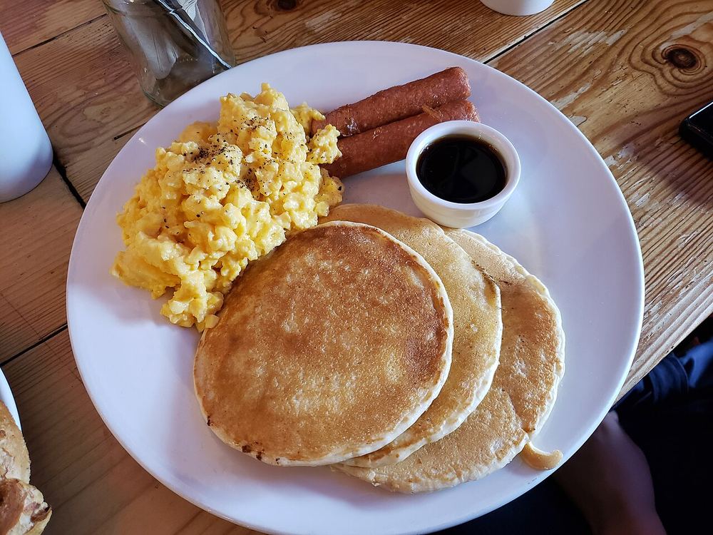 A breakfast plate of pancakes, scrambled eggs, and sausage