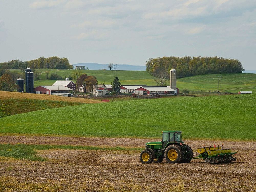 A green tractor working a field beside the Ridge Line Farm Equipment lot